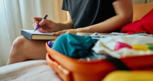ノートに書き込む人と荷造り中のオレンジ色のスーツケース
